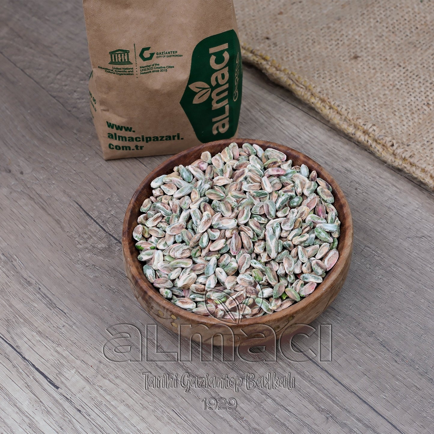 Tahta kasede Antep fıstık içi kuş gözü, yanında kahverengi bir ambalaj paketiyle birlikte duruyor.