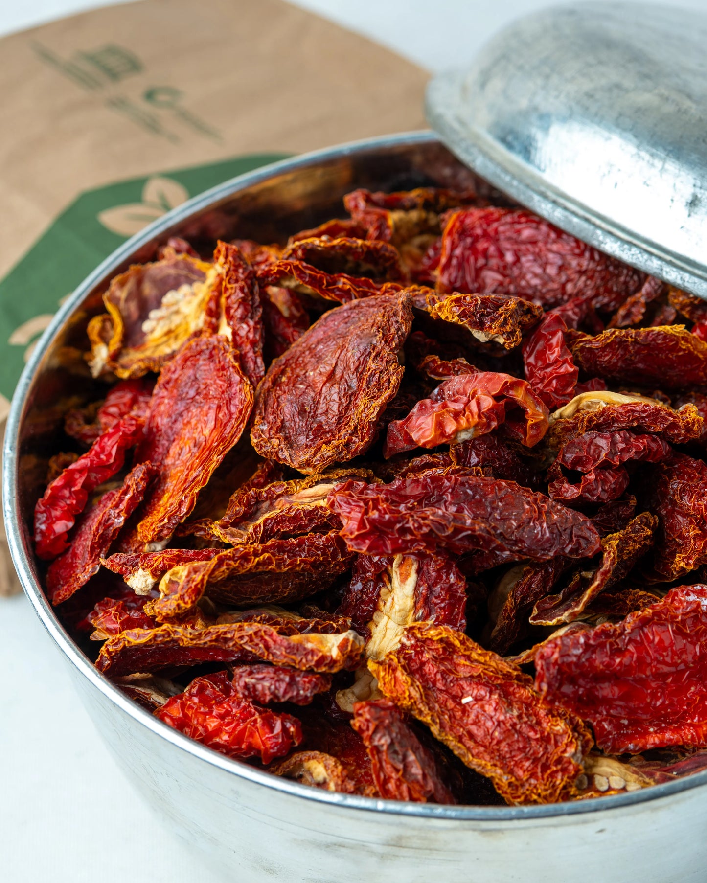 Metal kasede sunulan kuru domatesler ve Almacı Pazarı ambalajı, güneşte doğal tuzlama yöntemiyle kurutulmuş, kahvaltılık kırmızı domates kurusu.