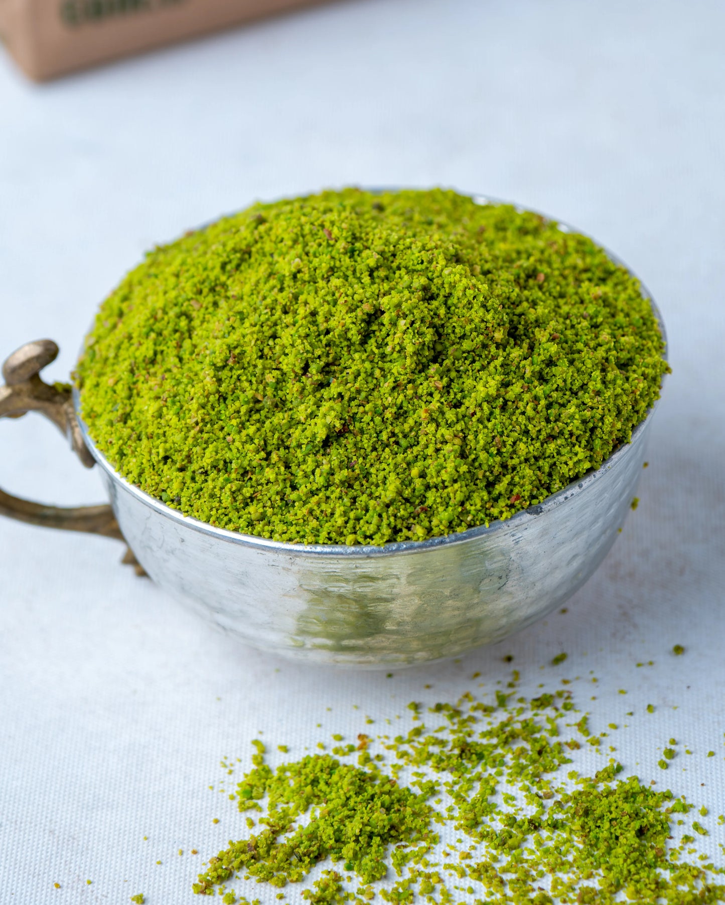 Yakından görünüm metal kasede toz Antep fıstığı, baklava ve künefe süslemesi için kullanılan canlı zümrüt yeşili, kabuksuz boz iç fıstık tozu.