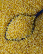 Yakından görünüm tahta kaşıkta sarı pilavlık bulgur, parlak altın rengi ve orta irilikte, domatesli pilav yapımı için doğal durum buğdayı.