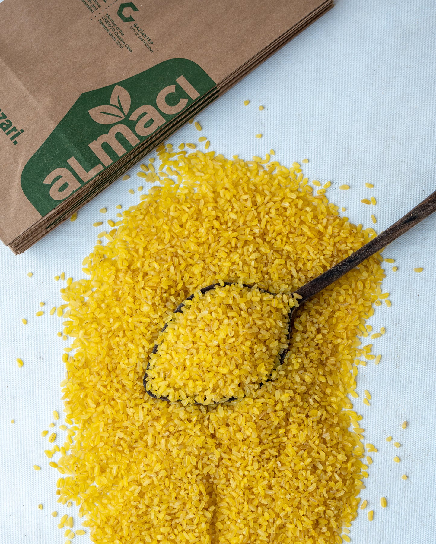 Yakından görünüm tahta kaşıkta sarı pilavlık bulgur, parlak altın rengi ve orta irilikte, domatesli pilav yapımı için doğal durum buğdayı.