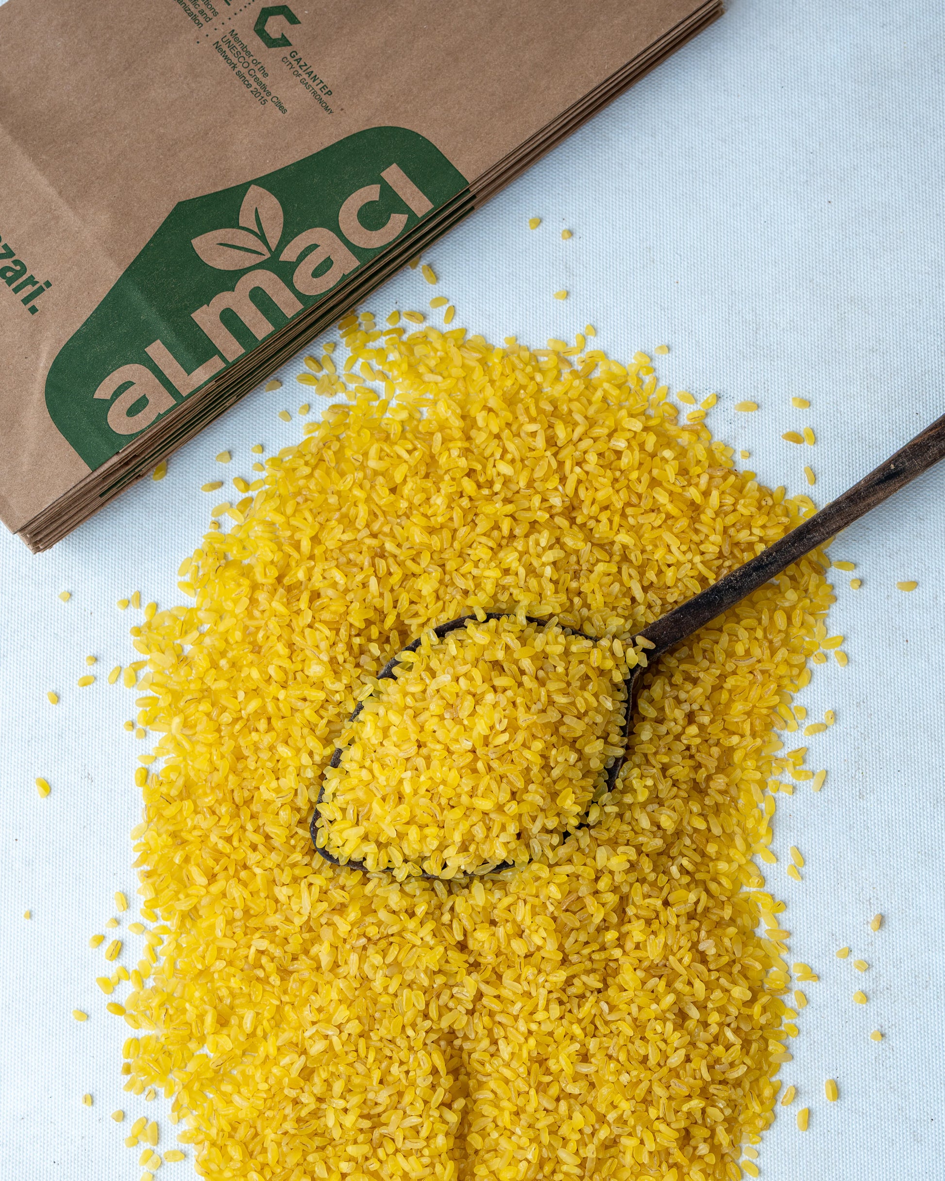 Yakından görünüm tahta kaşıkta sarı pilavlık bulgur, parlak altın rengi ve orta irilikte, domatesli pilav yapımı için doğal durum buğdayı.