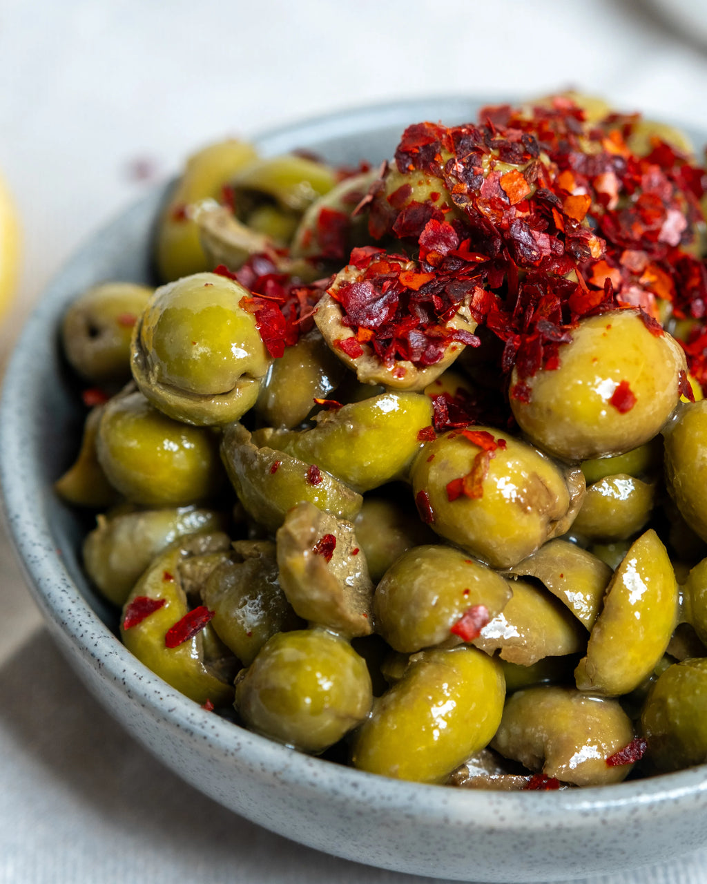 Kaşıkla pul biber dökülen çekirdeksiz yeşil zeytin, limon ve zeytinyağı eşliğinde hazırlanan iştah açıcı kahvaltılık sunum.