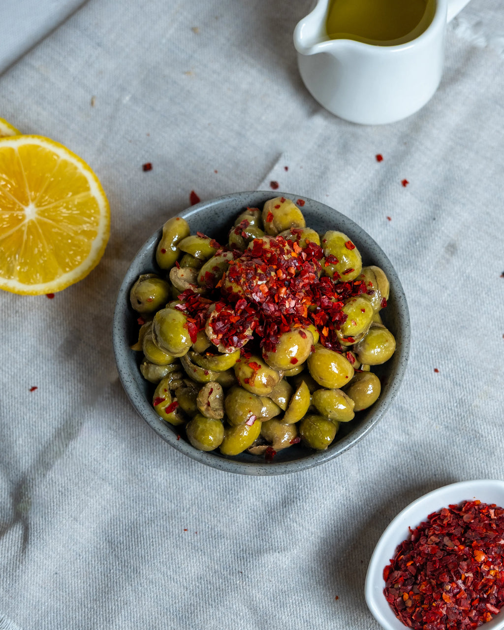 Kaşıkla pul biber dökülen çekirdeksiz yeşil zeytin, limon ve zeytinyağı eşliğinde hazırlanan iştah açıcı kahvaltılık sunum.