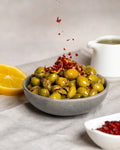 Kaşıkla pul biber dökülen çekirdeksiz yeşil zeytin, limon ve zeytinyağı eşliğinde hazırlanan iştah açıcı kahvaltılık sunum.