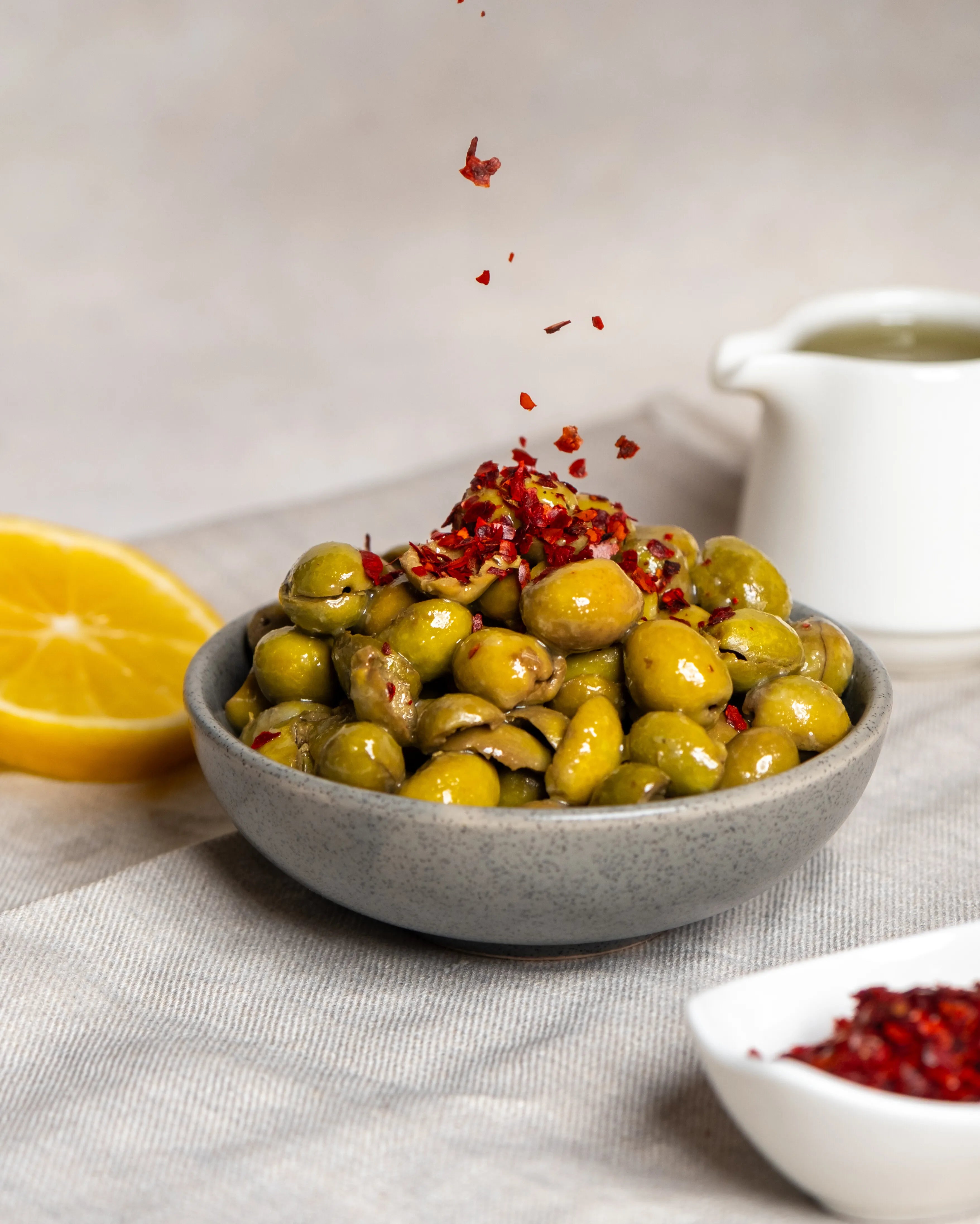 Kaşıkla pul biber dökülen çekirdeksiz yeşil zeytin, limon ve zeytinyağı eşliğinde hazırlanan iştah açıcı kahvaltılık sunum.