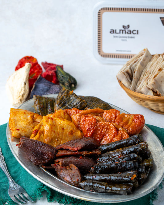 Metal tabakta sunulan karışık Antep dolması; patlıcan, biber, acur ve yaprak sarması çeşitleriyle, arka planda kuru sebze dizileriyle yöresel sunum.