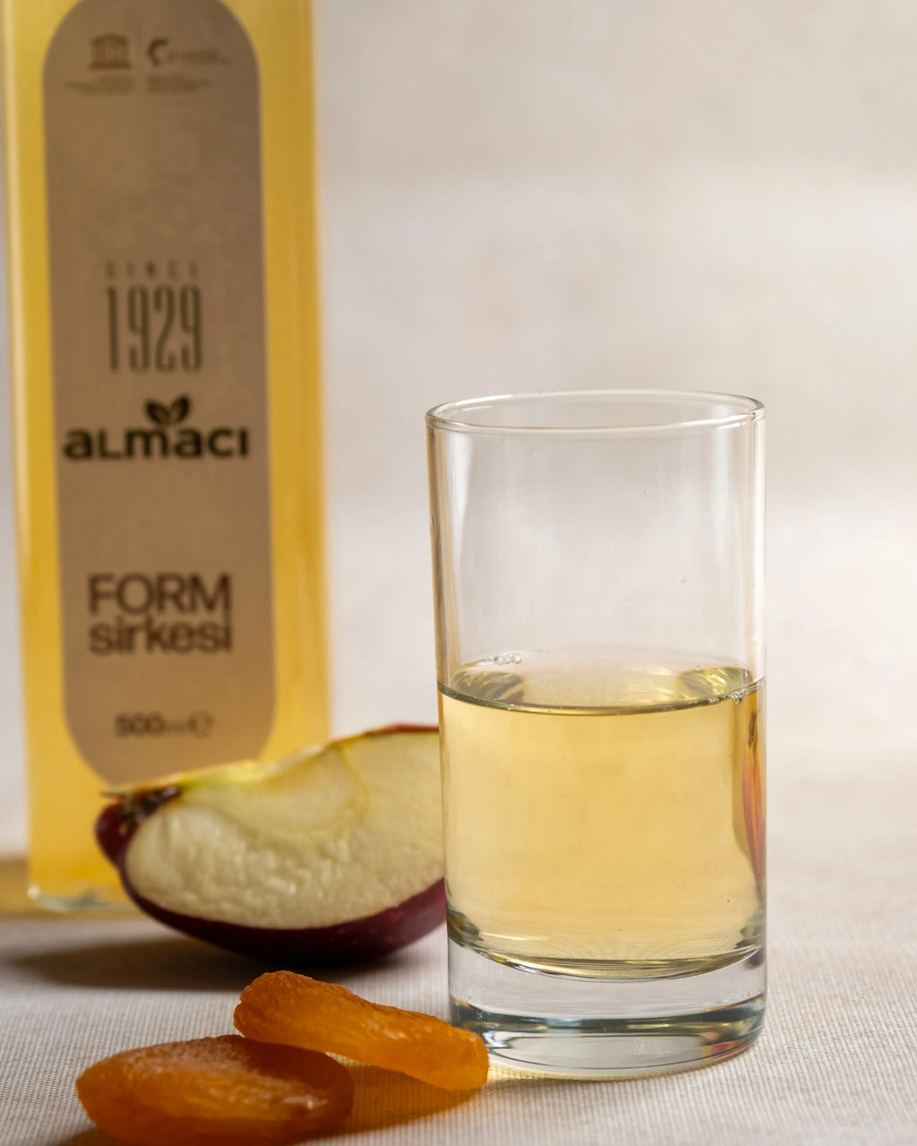 Almacı Pazarı Form Sirkesi şişeleri, yanında kuru kayısı ve elma dilimleriyle sunulan, metabolizma hızlandırıcı ve ödem atıcı doğal karışım sirke.