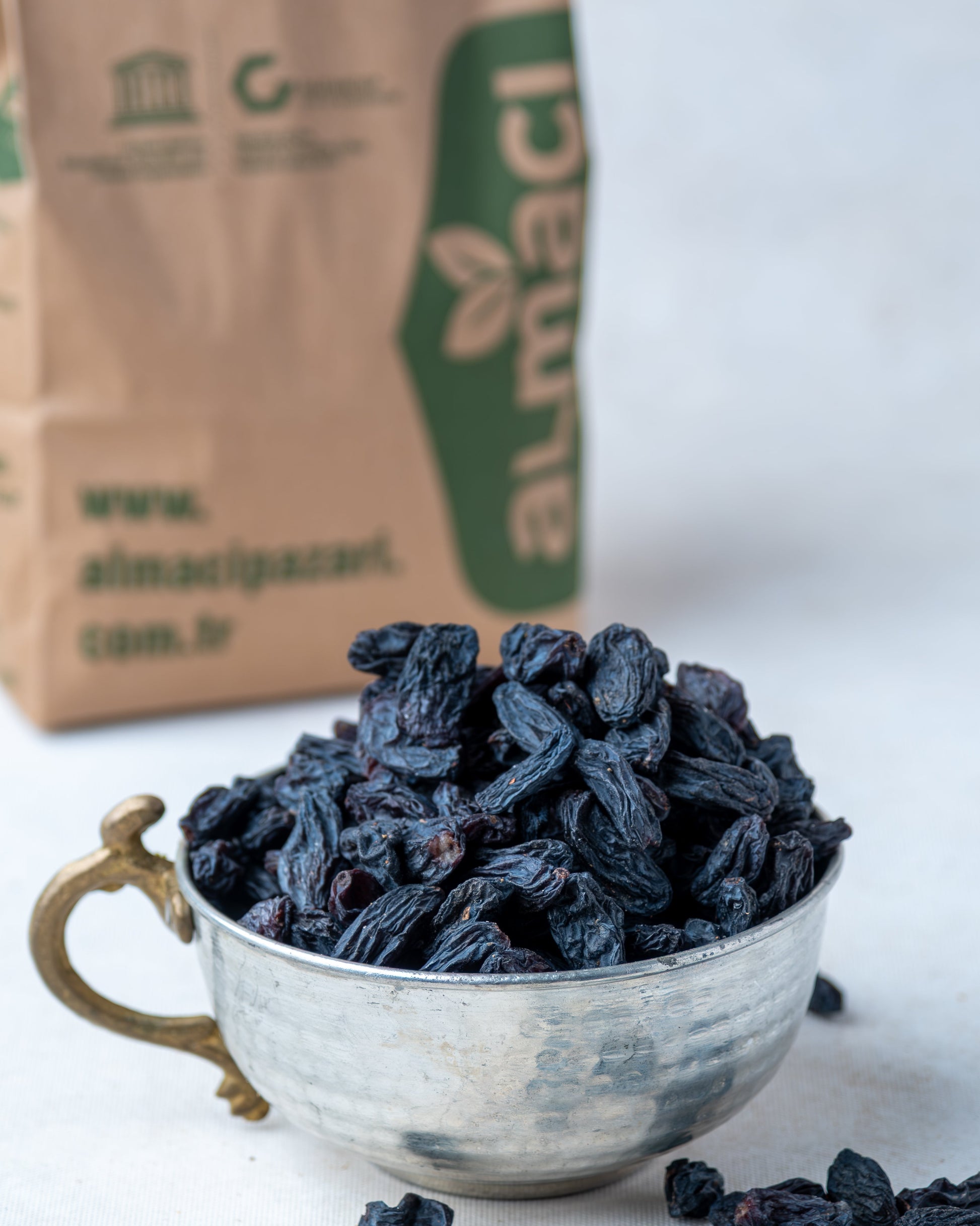 Metal kasede sunulan saplı siyah kuru üzüm ve arkada Almacı Pazarı paketi, kan yapıcı olarak bilinen doğal salkım kara üzüm.