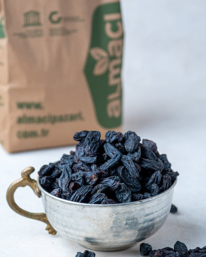 Metal kasede sunulan saplı siyah kuru üzüm ve arkada Almacı Pazarı paketi, kan yapıcı olarak bilinen doğal salkım kara üzüm.