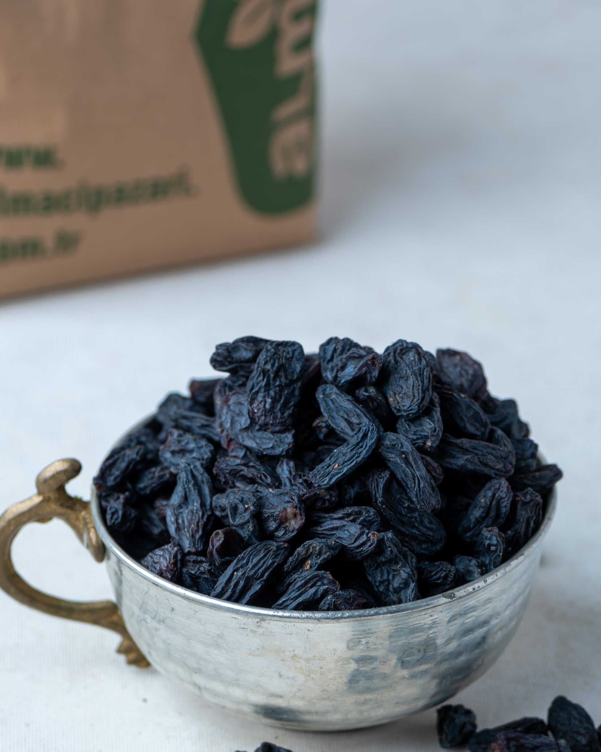 Metal kasede sunulan saplı siyah kuru üzüm ve arkada Almacı Pazarı paketi, kan yapıcı olarak bilinen doğal salkım kara üzüm.