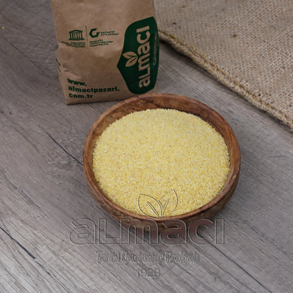 Tahta kasede duran köftelik bulgur, bir masa üzerinde sergileniyor. Yanında, üzerinde “almacipazari.com.tr” yazılı bir kağıt torba bulunuyor. 