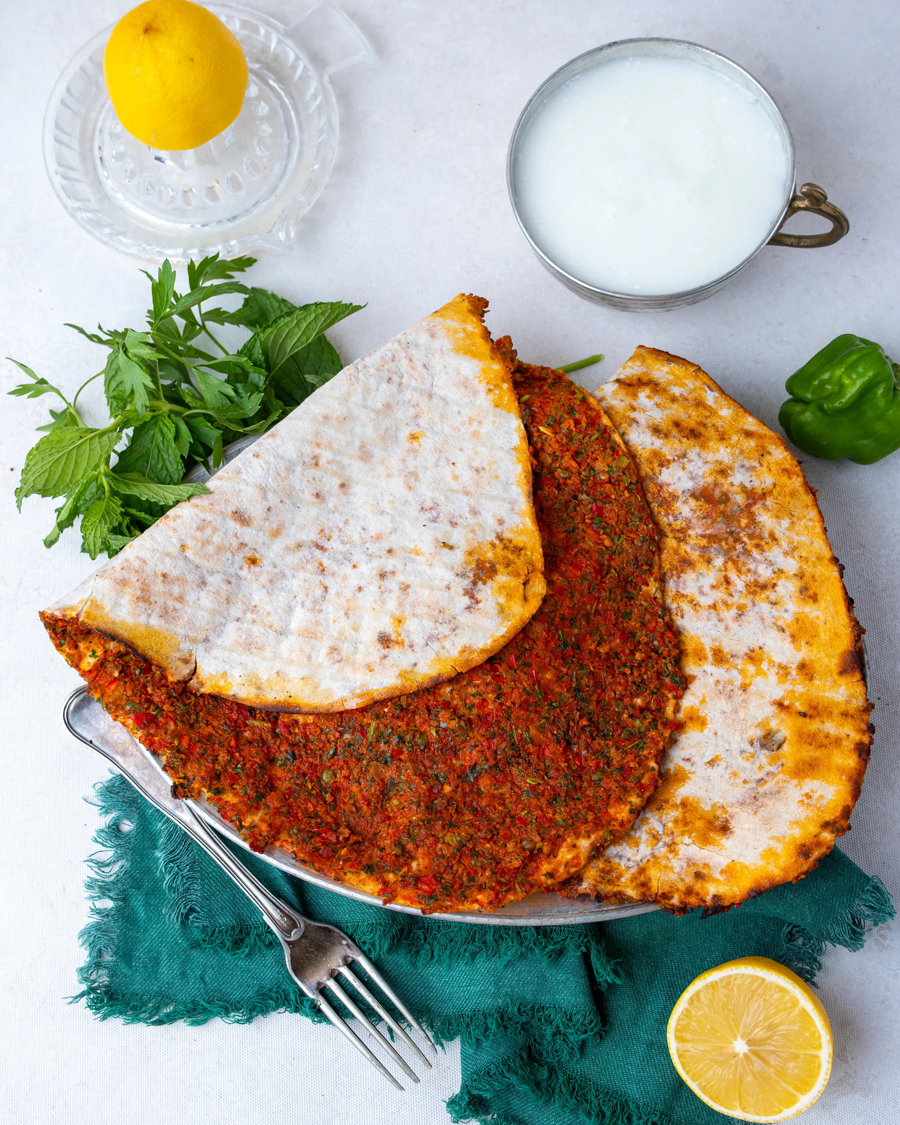 Metal tabakta servis edilen ince hamurlu Gaziantep lahmacunu, yanında bol köpüklü ayran, limon ve taze yeşilliklerle sunulan taş fırın lezzeti.