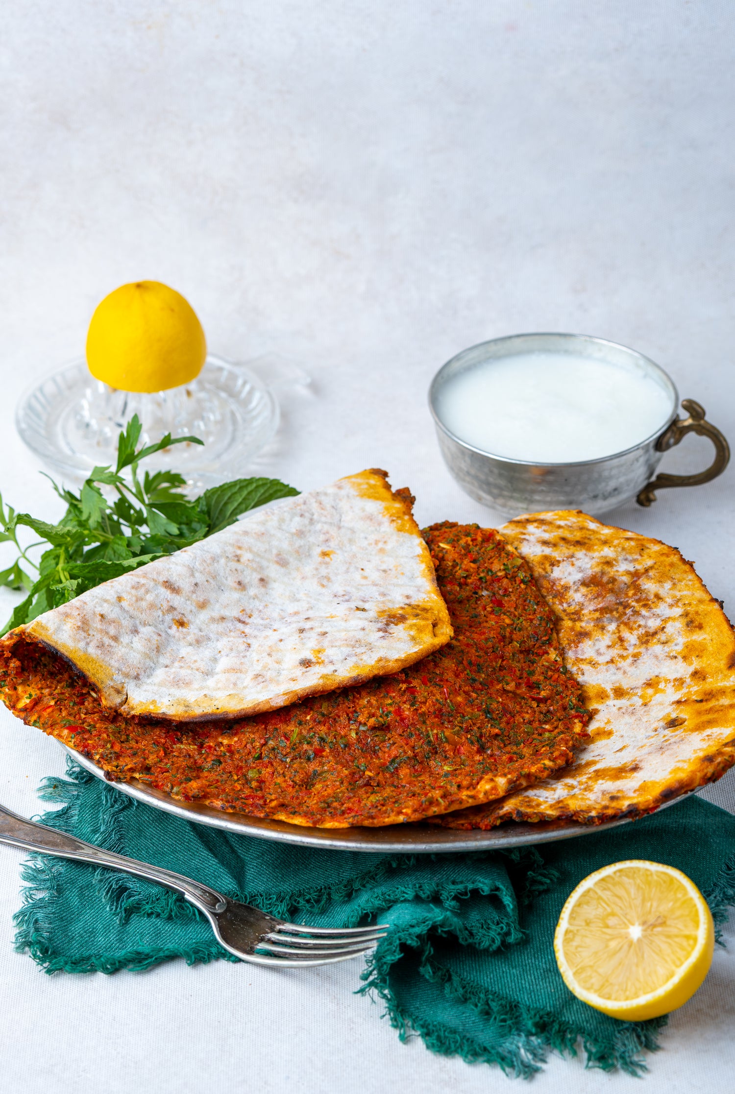 Metal tabakta servis edilen ince hamurlu Gaziantep lahmacunu, yanında bol köpüklü ayran, limon ve taze yeşilliklerle sunulan taş fırın lezzeti.