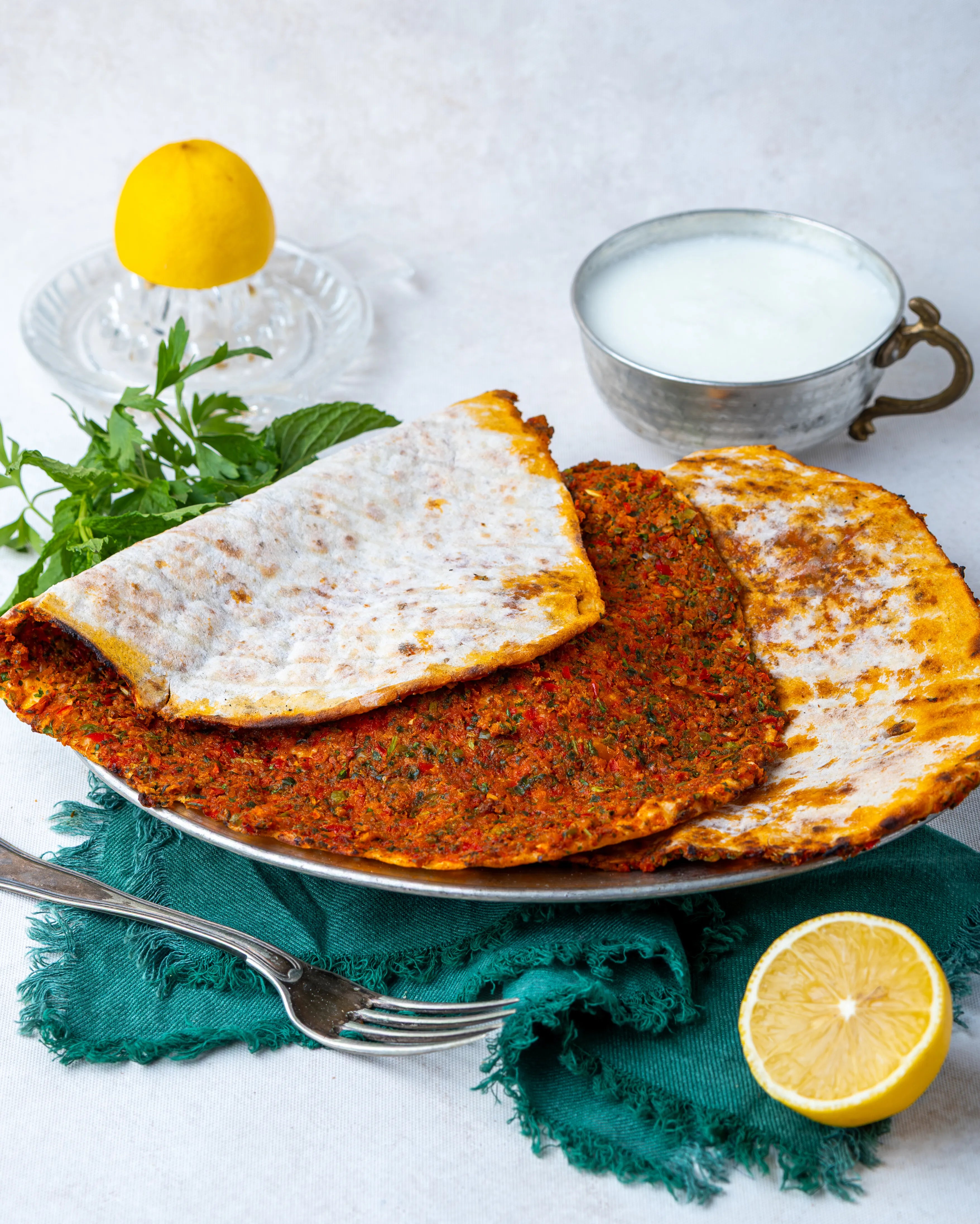 Metal tabakta servis edilen ince hamurlu Gaziantep lahmacunu, yanında bol köpüklü ayran, limon ve taze yeşilliklerle sunulan taş fırın lezzeti.