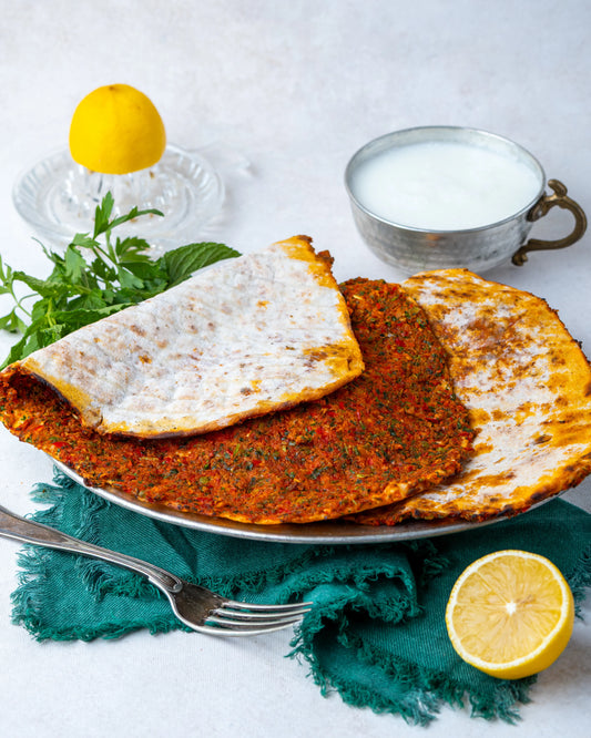 Metal tabakta servis edilen ince hamurlu Gaziantep lahmacunu, yanında bol köpüklü ayran, limon ve taze yeşilliklerle sunulan taş fırın lezzeti.