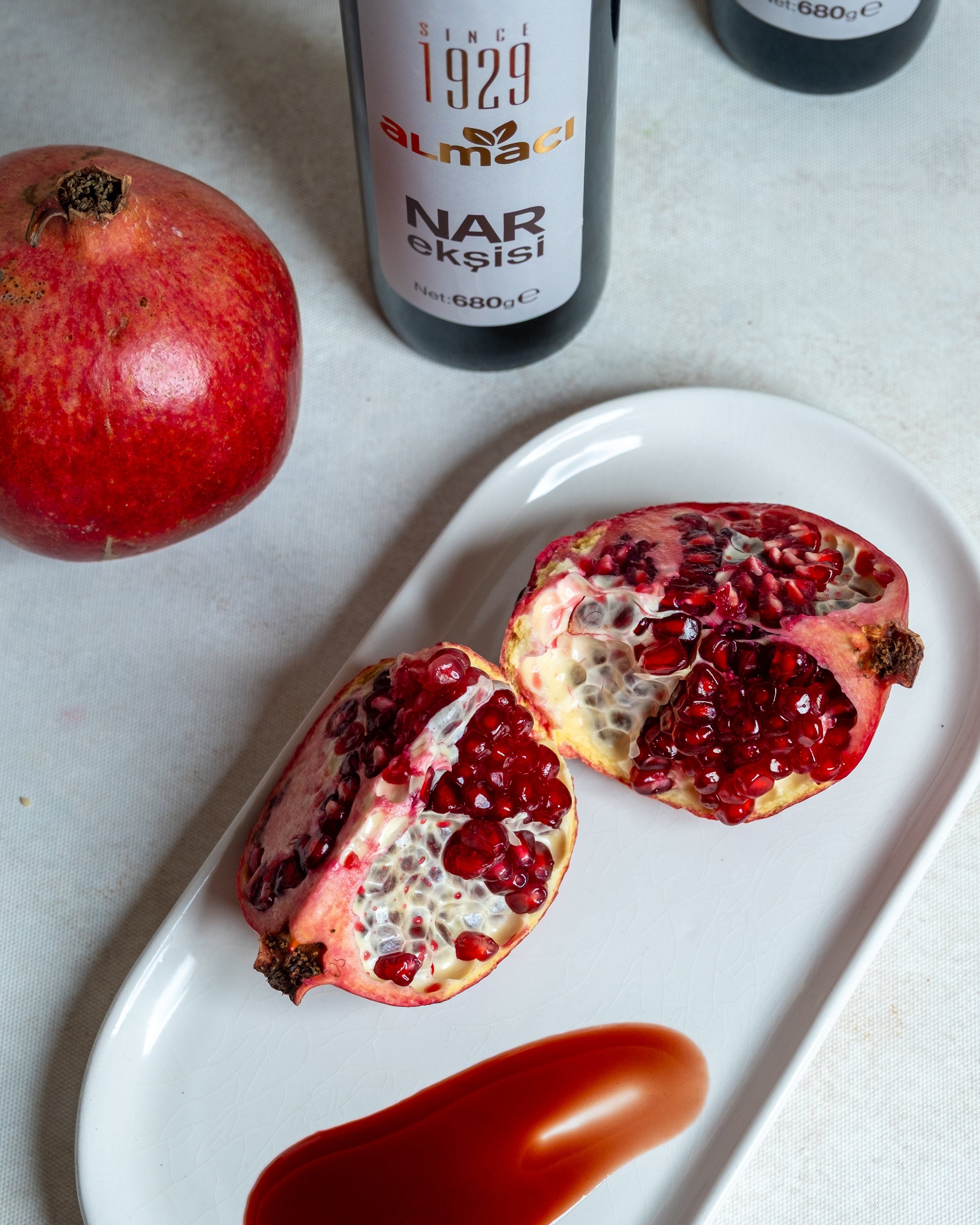 Beyaz tabakta koyu kıvamlı nar ekşisi sunumu ve taze nar, salatalar ve çiğ köfte için katkısız doğal nar suyu konsantresi.