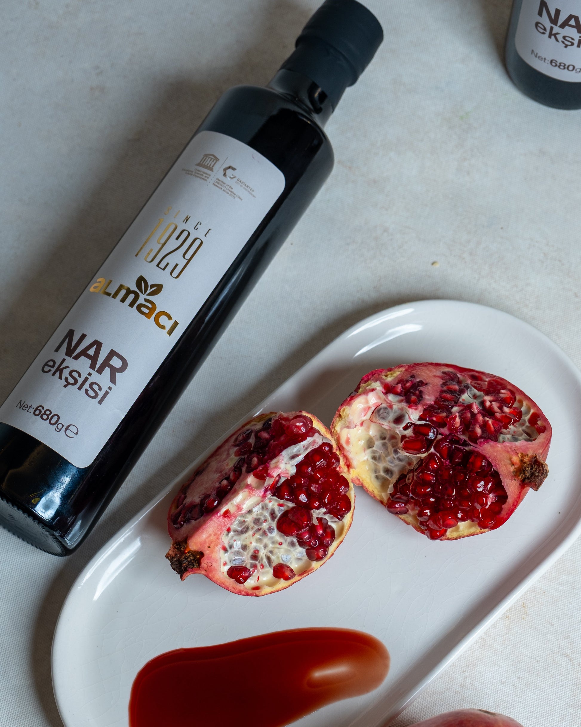 Beyaz tabakta koyu kıvamlı nar ekşisi sunumu ve taze nar, salatalar ve çiğ köfte için katkısız doğal nar suyu konsantresi.