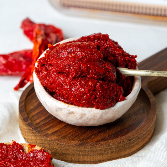 Ahşap sunumda kase içinde acı biber salçası, arka planda hammaddesi olan kuru kırmızı biberlerle sunulan, koyu kıvamlı Antep usulü salça.