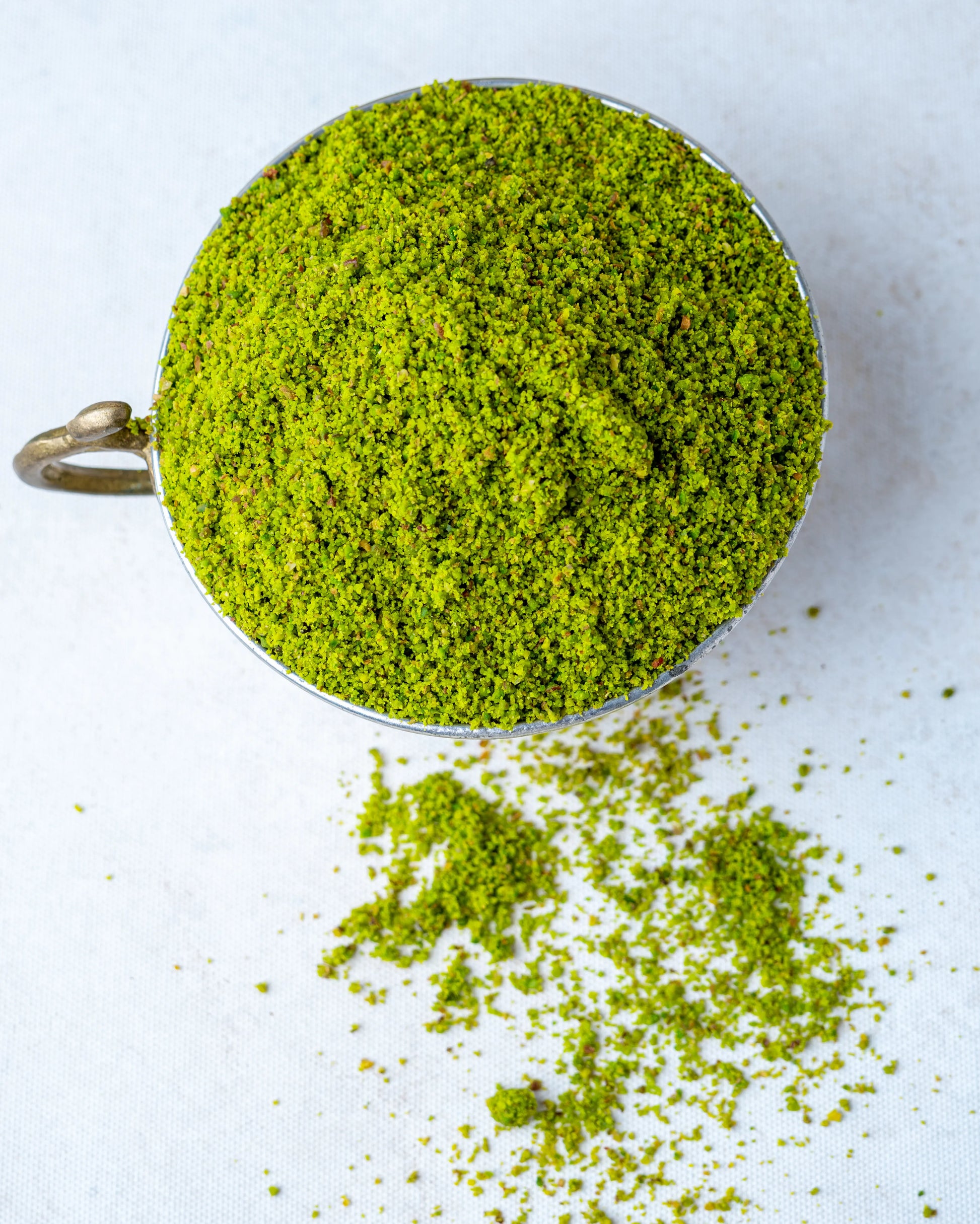 Yakından görünüm metal kasede toz Antep fıstığı, baklava ve künefe süslemesi için kullanılan canlı zümrüt yeşili, kabuksuz boz iç fıstık tozu.