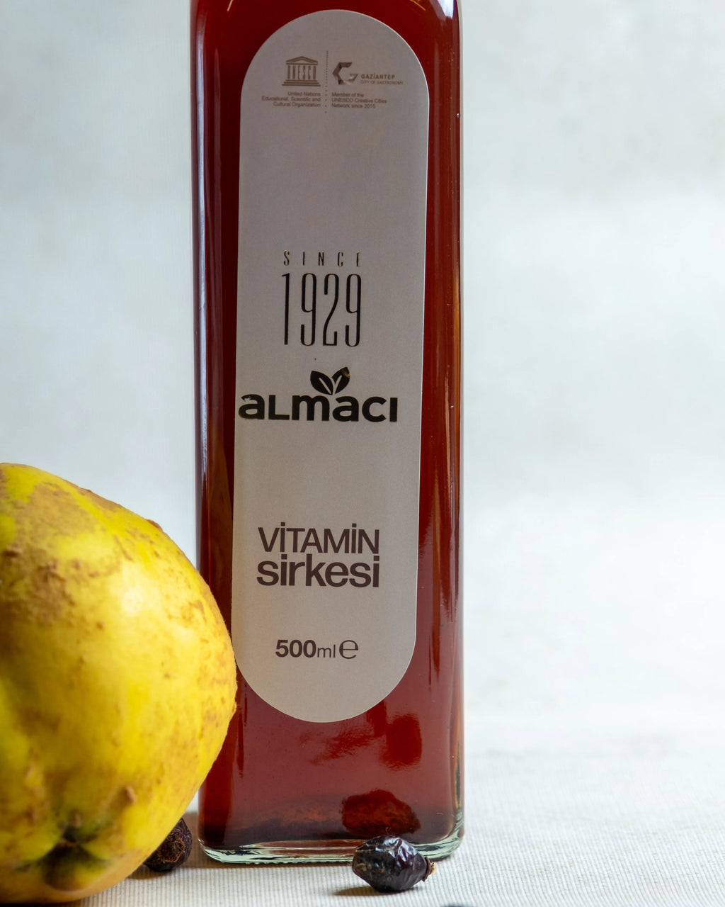Almacı Pazarı vitamin sirkesi şişeleri, yanında taze ayva ve kuru kuşburnu ile sunulan, C vitamini deposu bağışıklık güçlendirici karışım sirke.