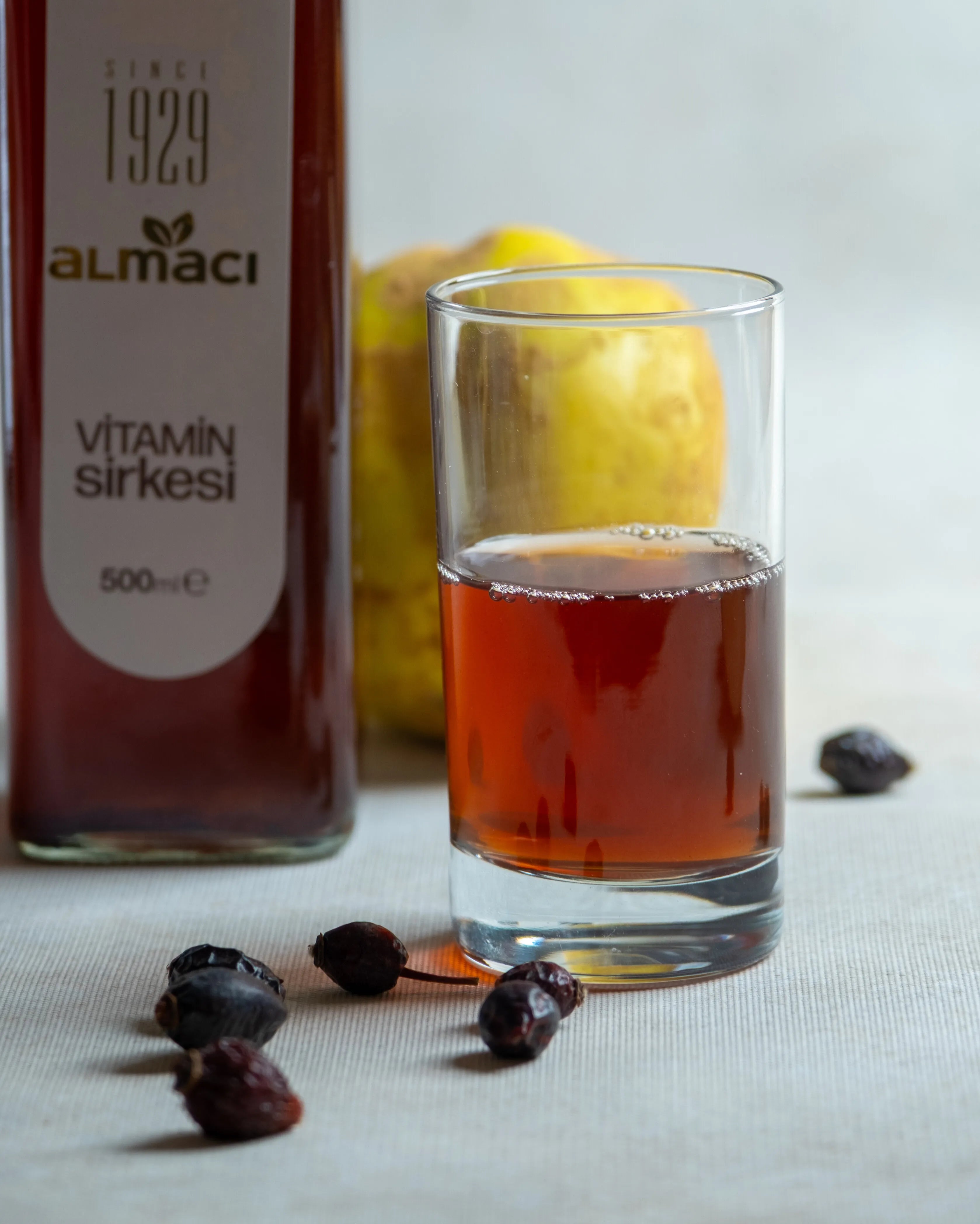 Almacı Pazarı vitamin sirkesi şişeleri, yanında taze ayva ve kuru kuşburnu ile sunulan, C vitamini deposu bağışıklık güçlendirici karışım sirke.